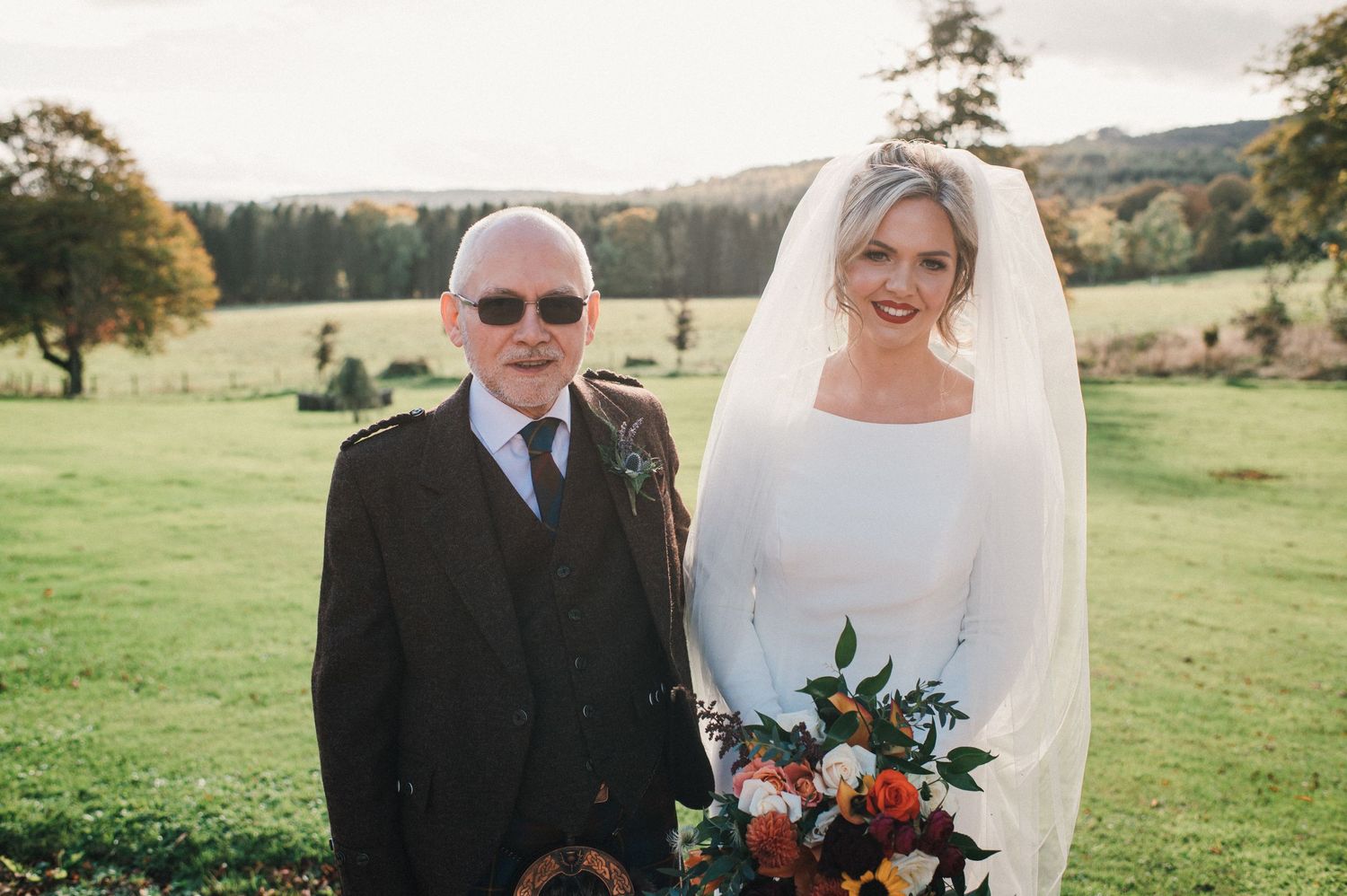 Wedding portrait in an autumn field with elegant floral bouquet featuring seasonal blooms.