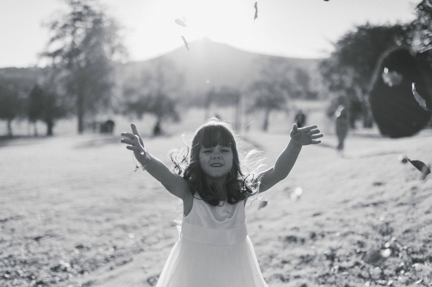 A joyful child in white dress plays outdoors in black and white photography.