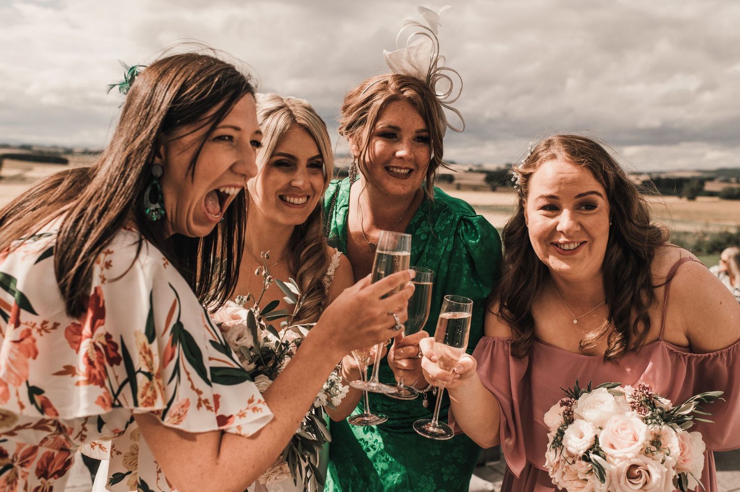 Group of friends in floral and colorful dresses toasting with champagne glasses at an outdoor event.