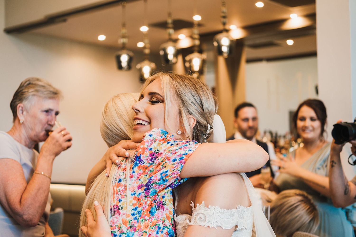 Joyful celebration captured at an indoor wedding reception with guests embracing.