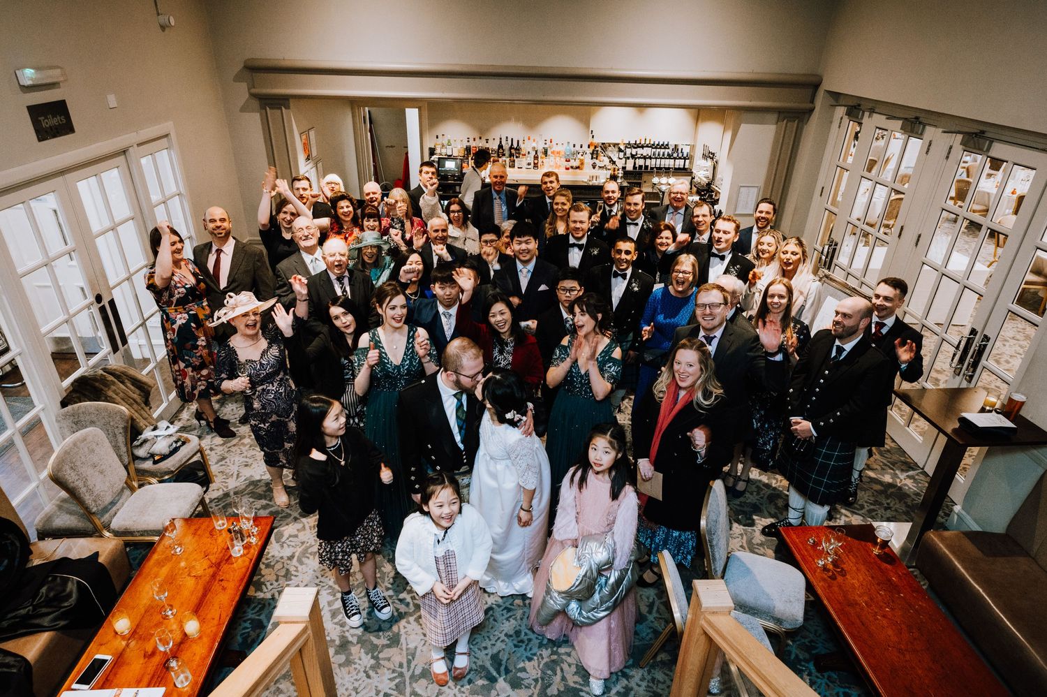 Overhead view of wedding guests gathered for a group photo in an elegant indoor venue.