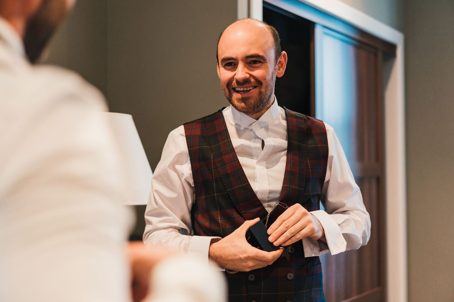 Groom wearing a classic white shirt and patterned vest smiles while preparing for the ceremony.
