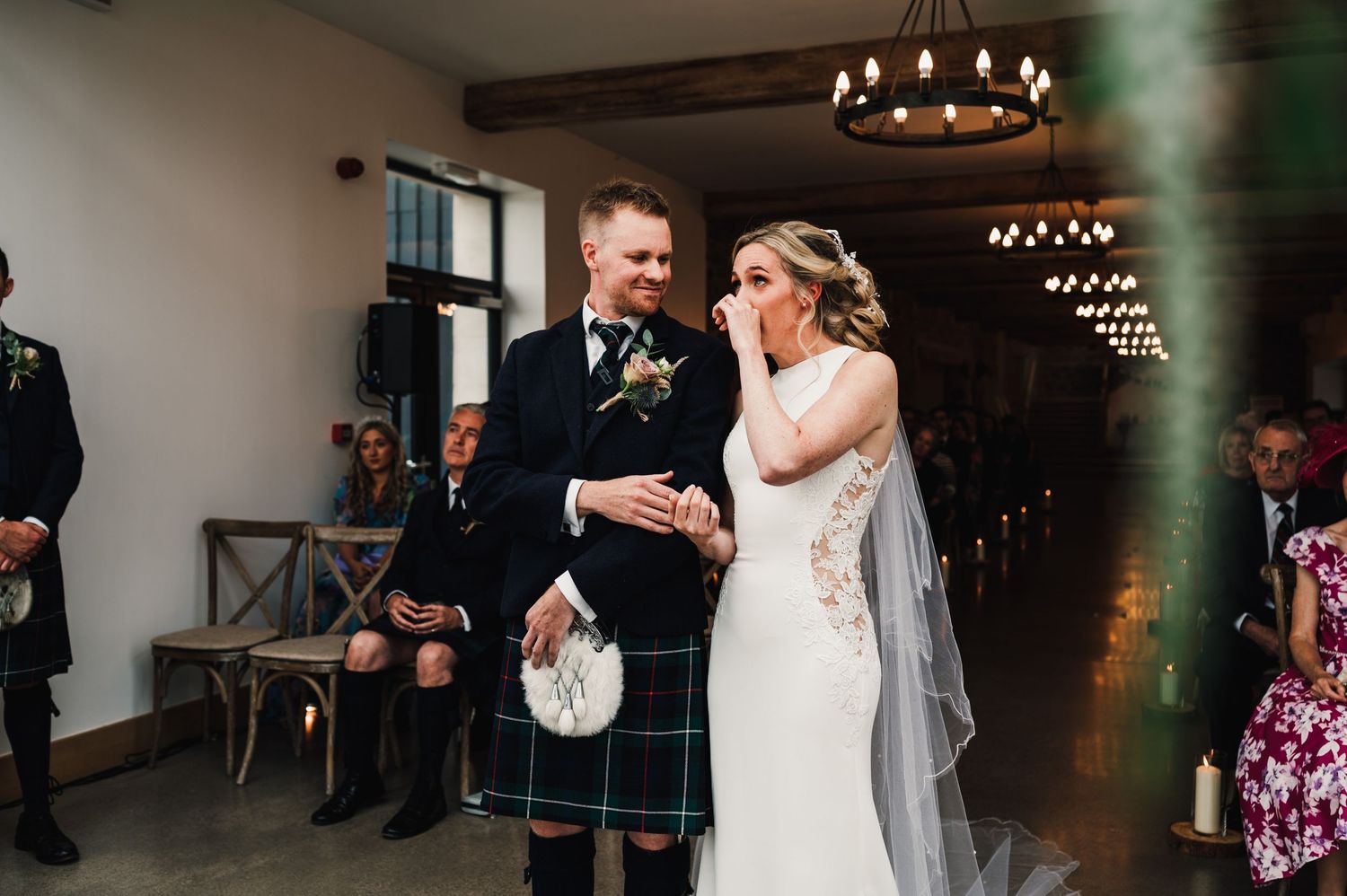 Joyful couple sharing a moment during their indoor Scottish wedding ceremony with kilts and chandeliers.