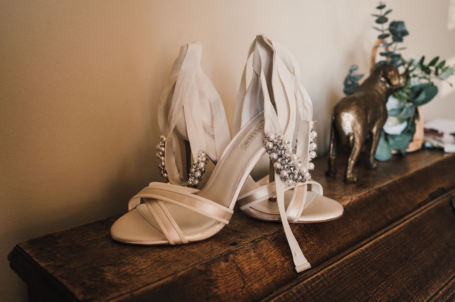 Elegant white bridal shoes with crystal embellishments displayed on wooden surface.