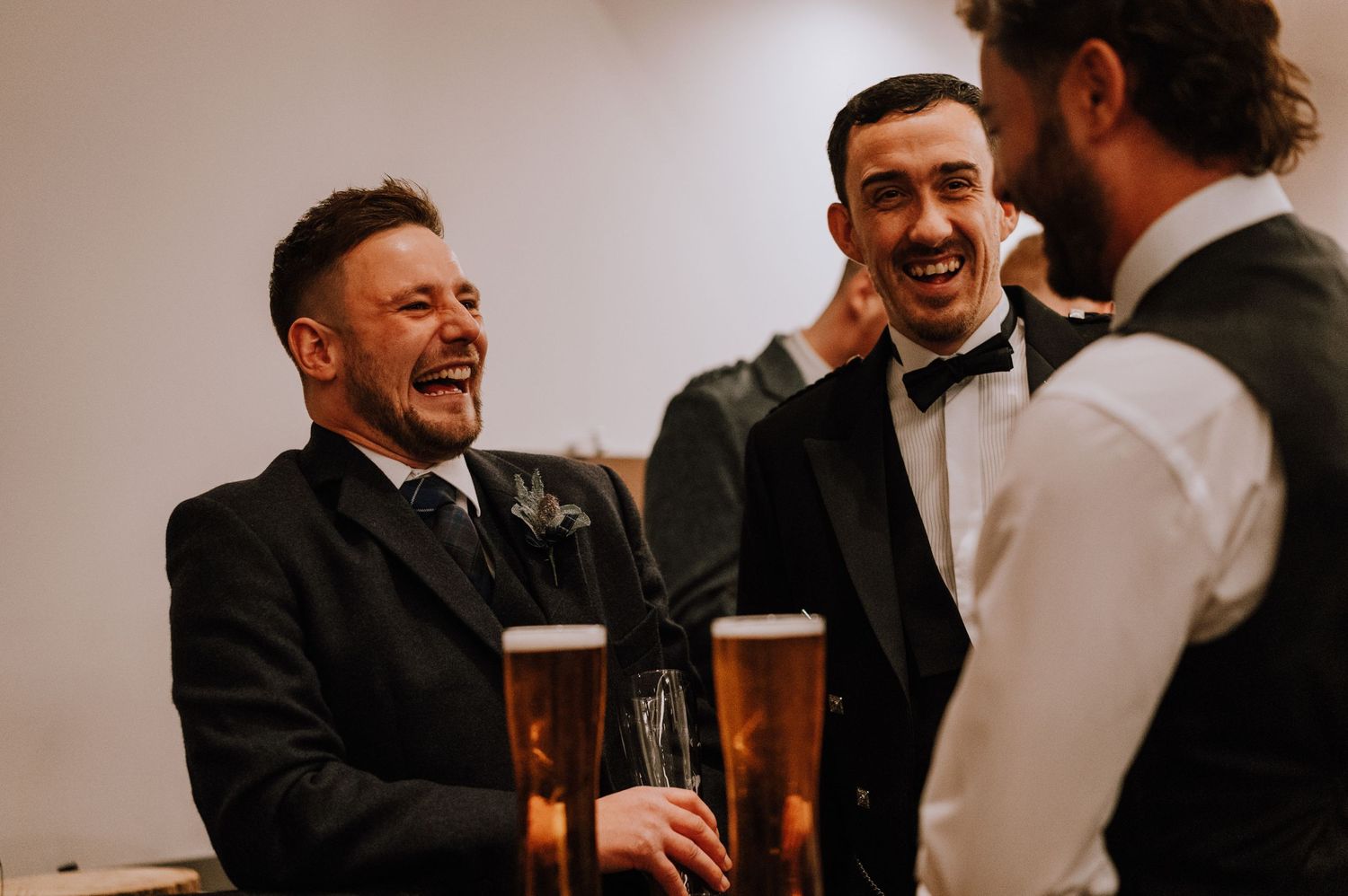 Guests share laughs and beers at a formal wedding celebration.