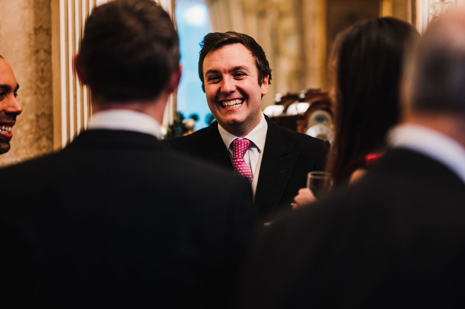 A guest smiles warmly during conversation at an elegant indoor gathering.