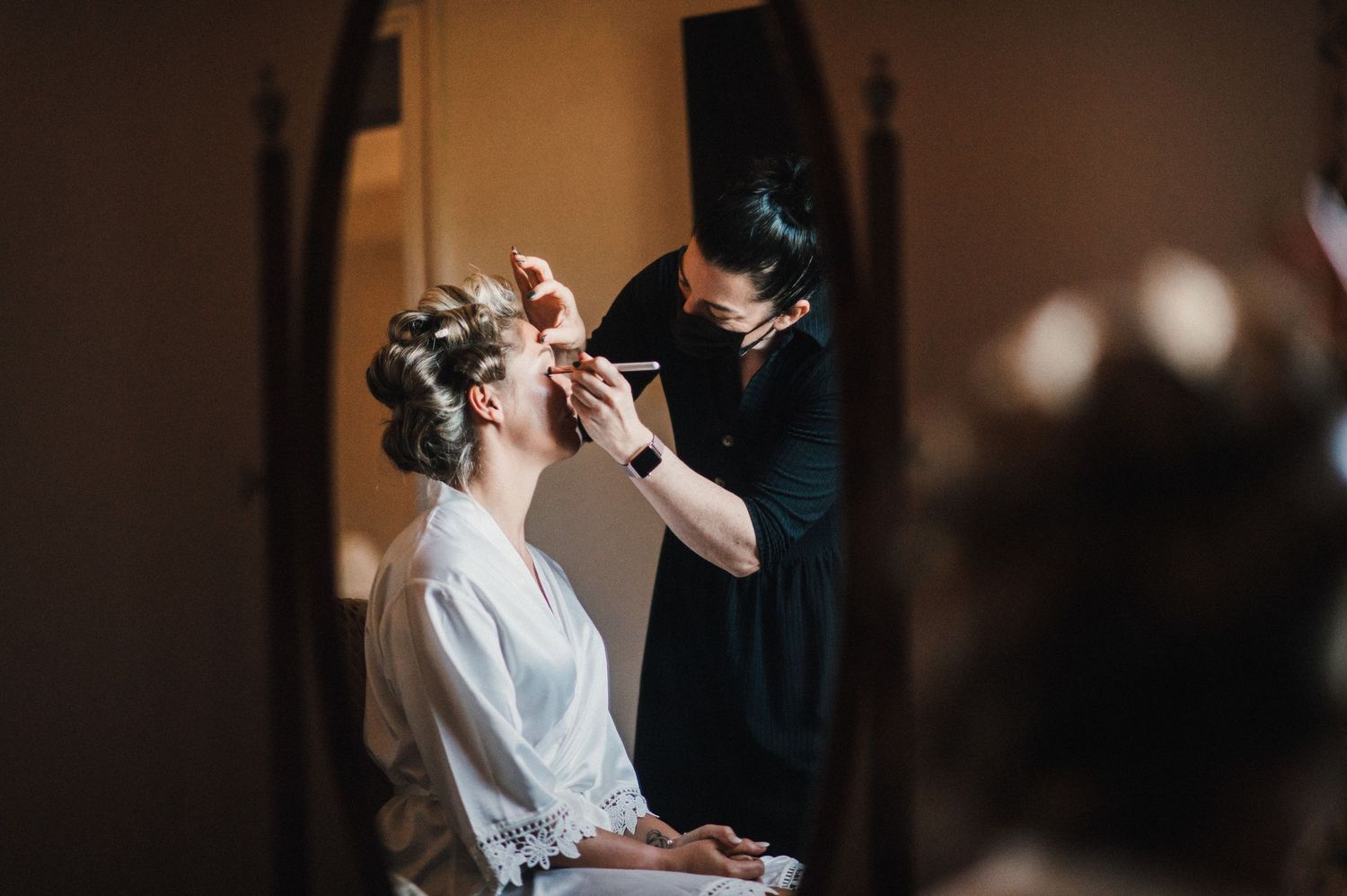 Professional makeup artist working on client's makeup in dimly lit room.