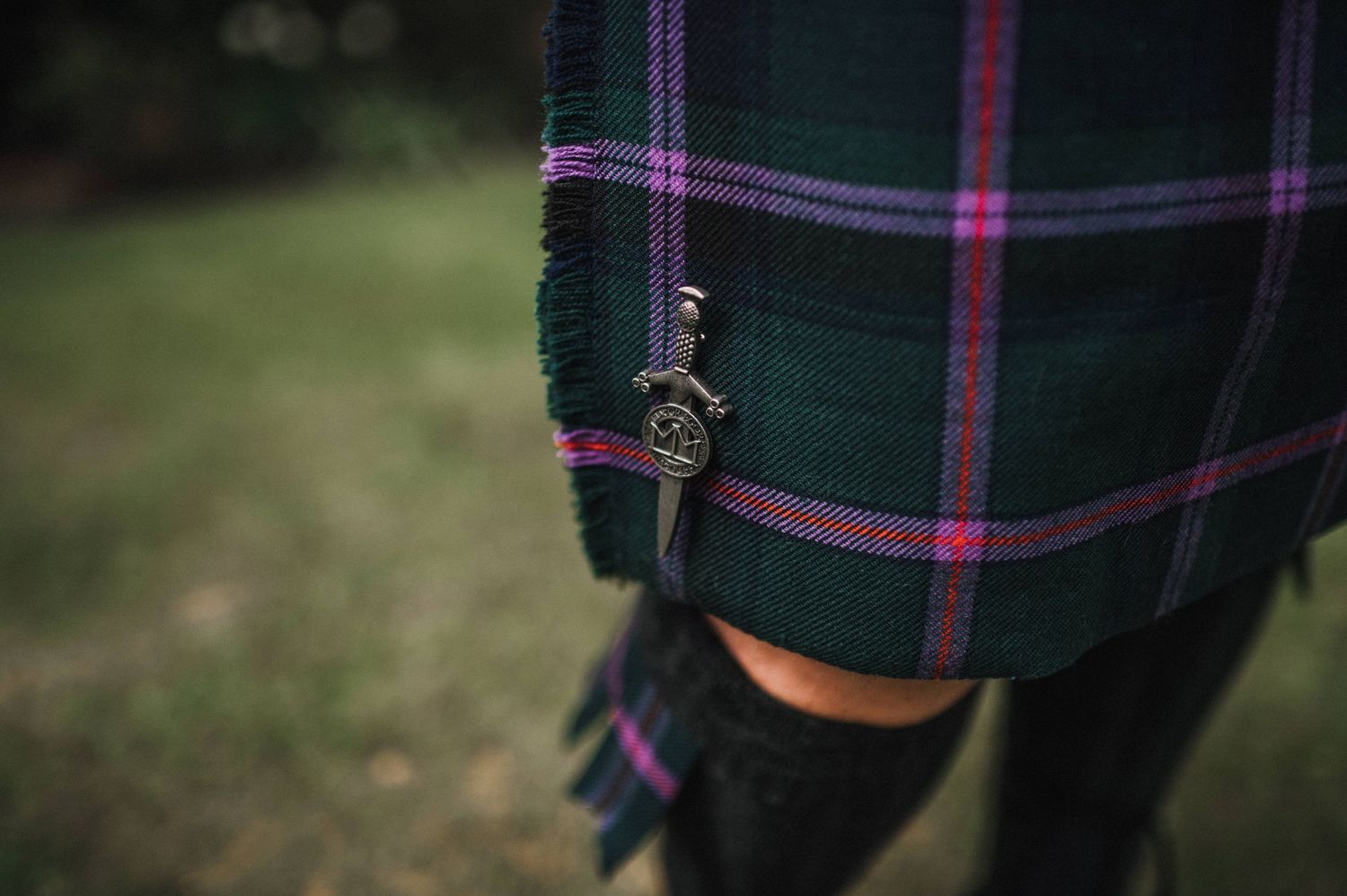 Person in Scottish formal wear sits on a bench reading documents.