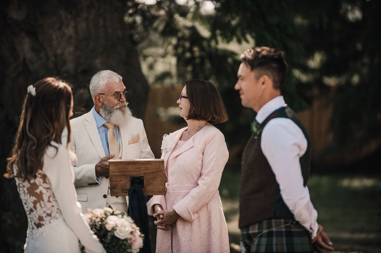 Outdoor wedding ceremony with officiant and couple in Scottish wedding attire.