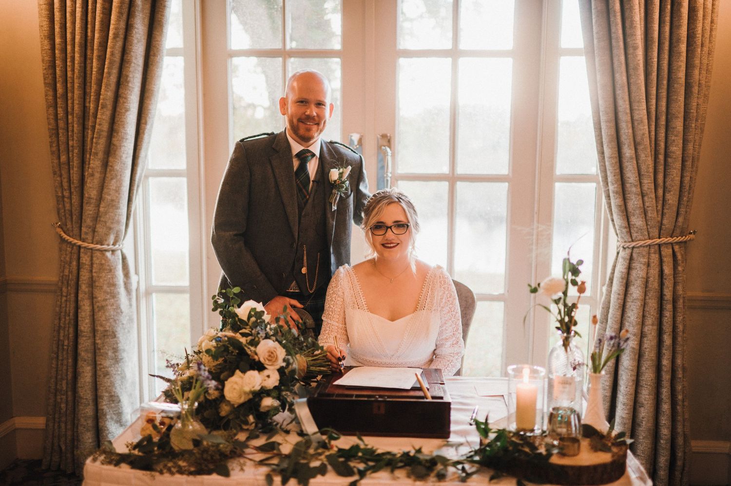 Couple at their wedding signing table decorated with floral arrangements and candles.