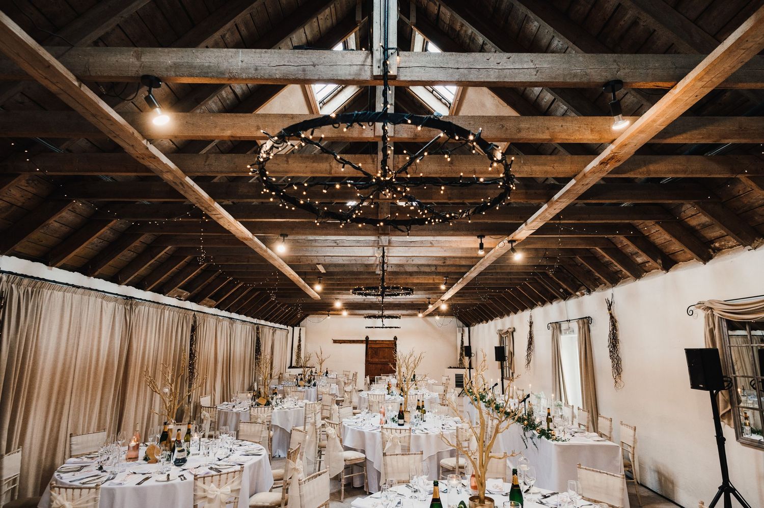 Rustic barn wedding reception venue with exposed wooden beams and elegant white table settings.