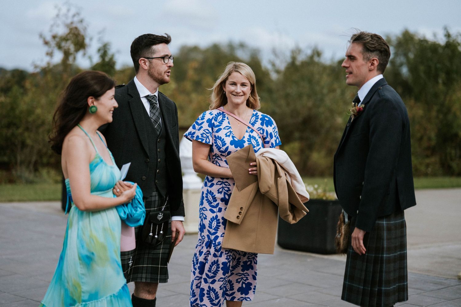 Small group chatting at outdoor wedding with men in traditional Scottish kilts.