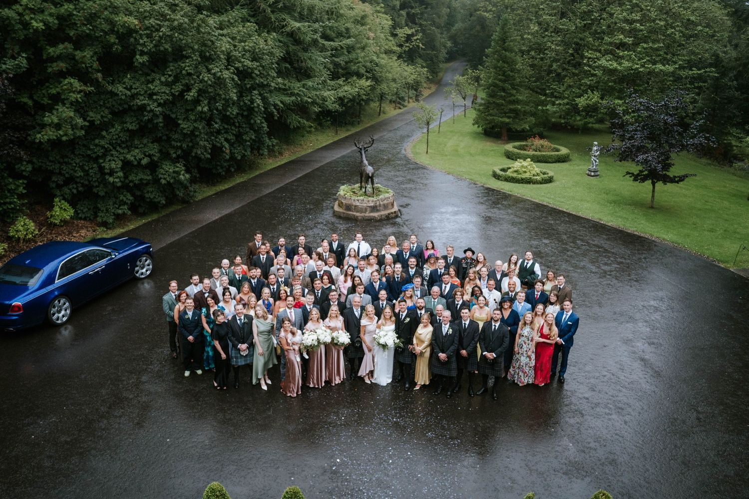 Large wedding group photo taken outdoors with castle-like building in background.
