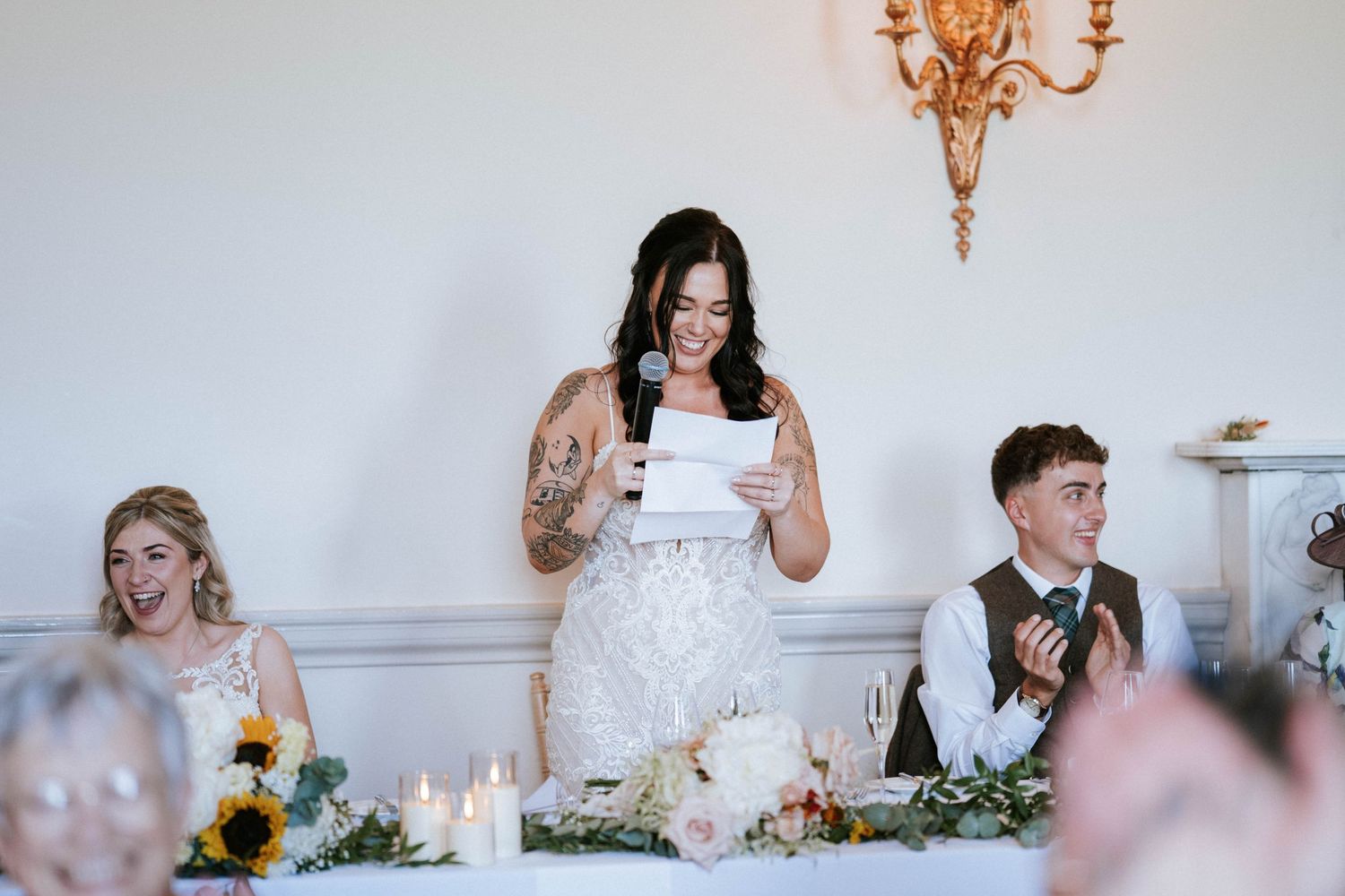 Fasque Castle Wedding Photography. Wedding party members engage in animated conversation at decorated reception table.