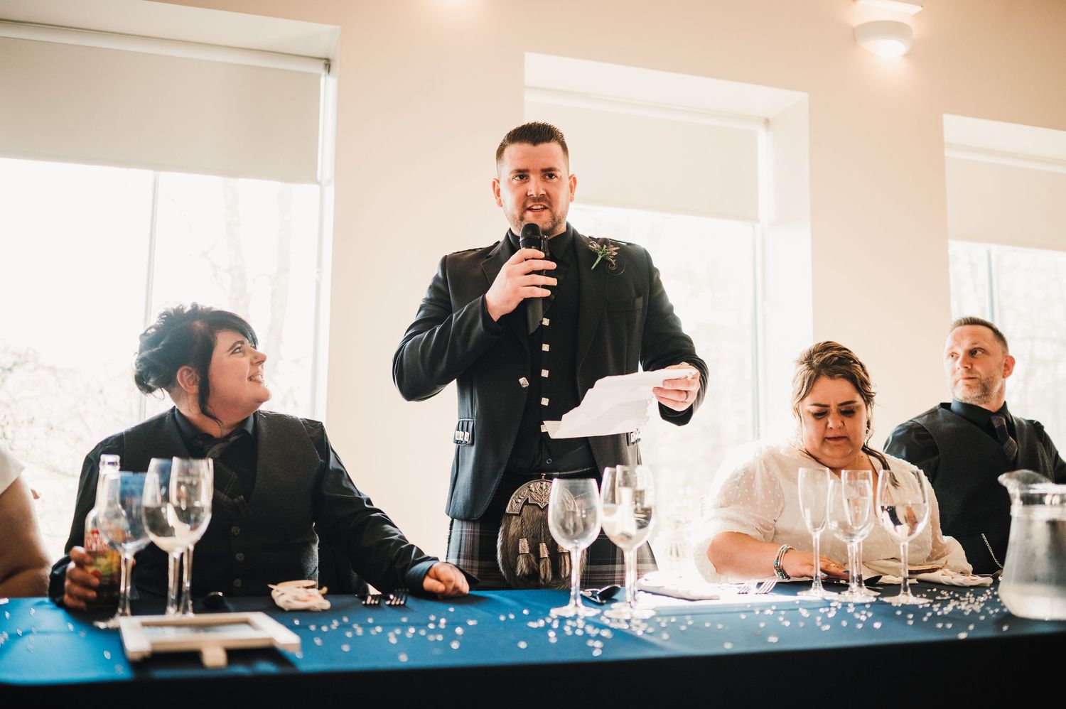 Logie House Wedding Photography. Wedding reception speakers address guests at a formal table decorated with blue accents.