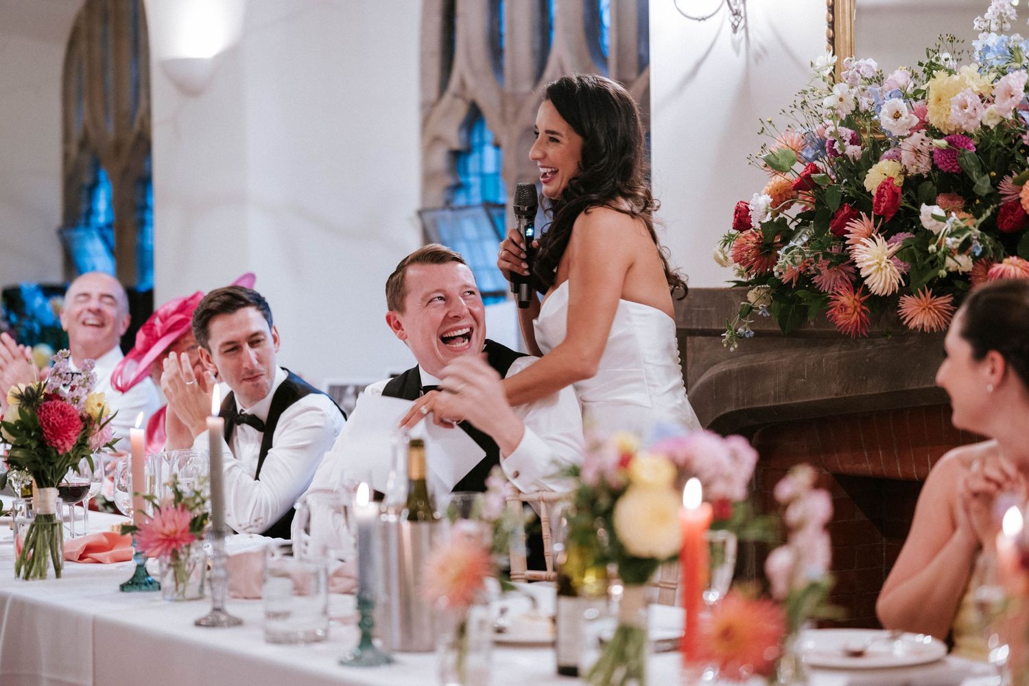 Wedding guests enjoying speeches at tables decorated with pink floral centerpieces.