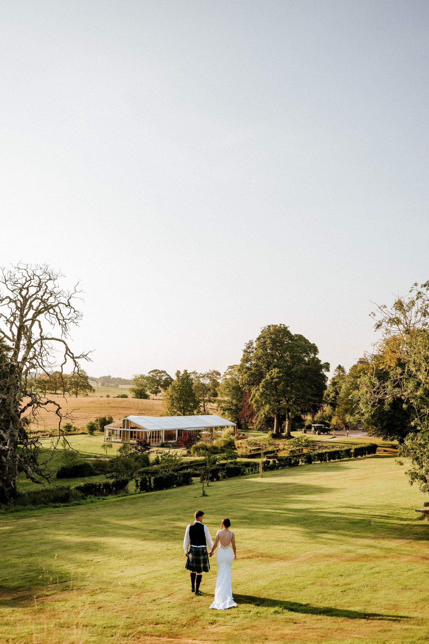 Aberdeen Wedding Photography. Couple walks across expansive green lawn of countryside wedding venue.