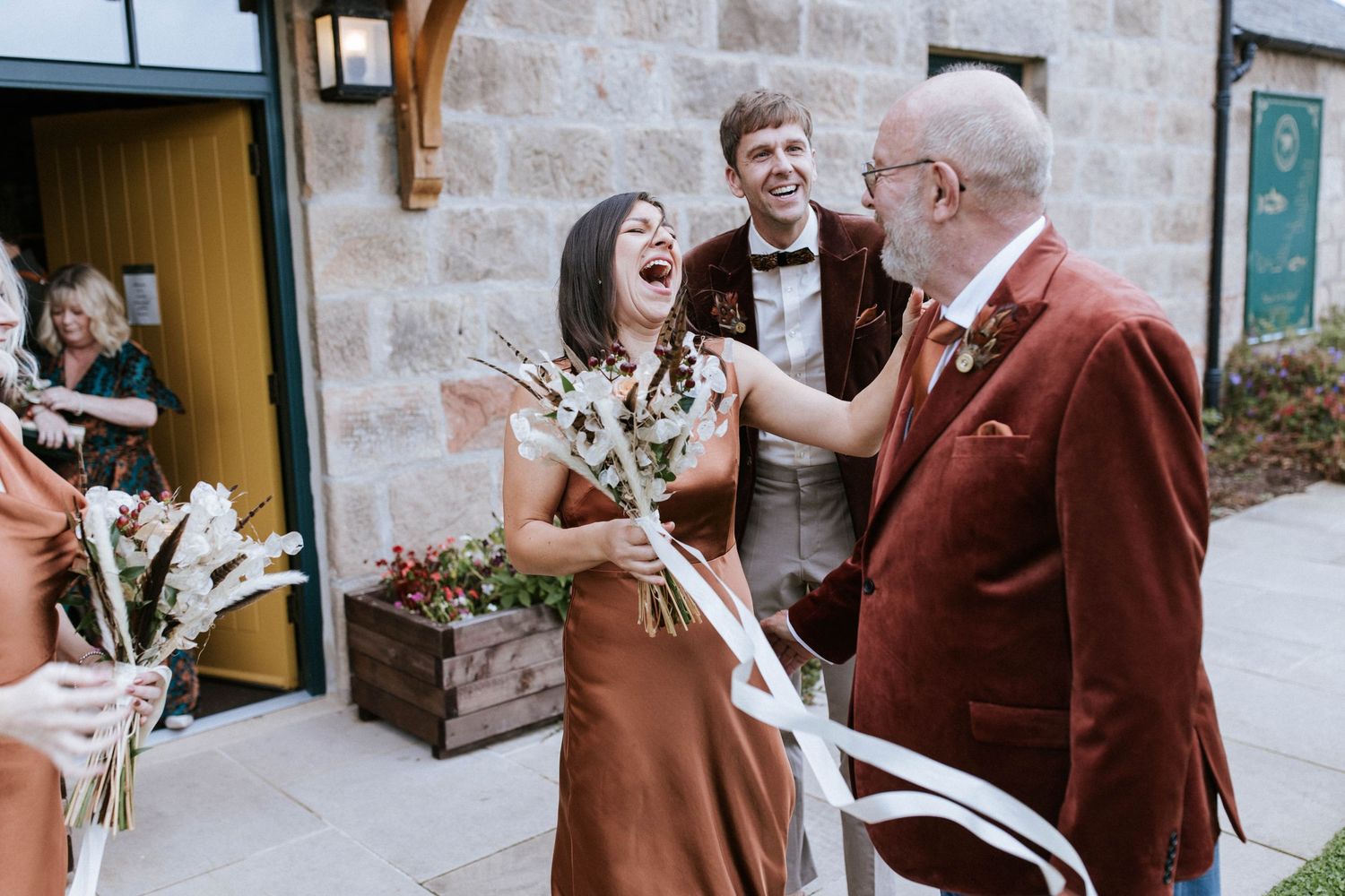 Wedding guests celebrating and laughing together against a stone wall backdrop.