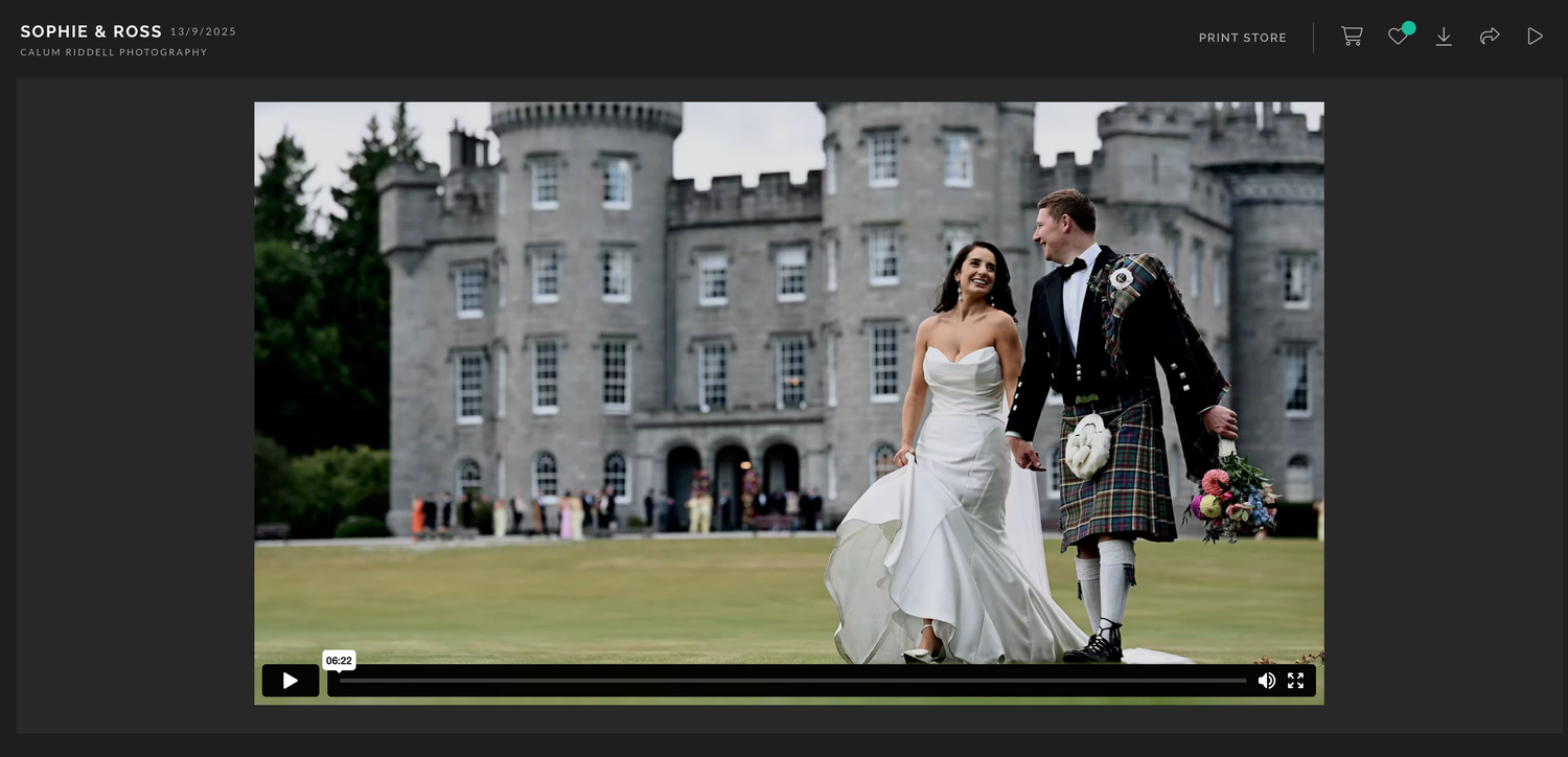 A wedding couple walks along a scenic path at an elegant estate venue with stone buildings in the background.