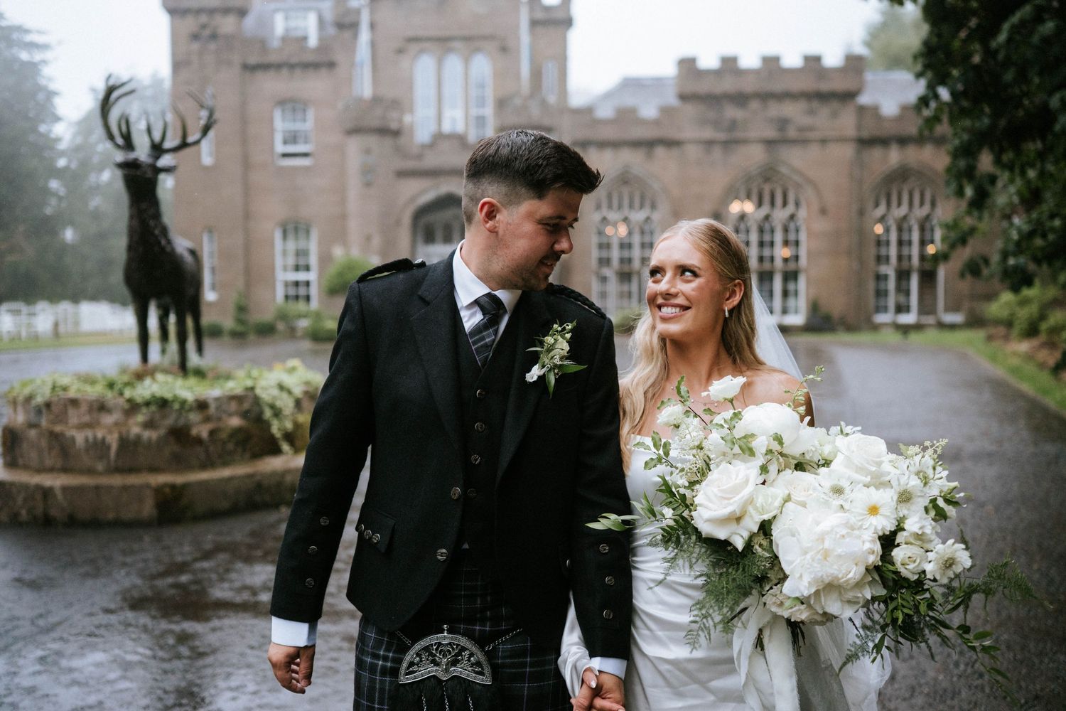 Wedding couple walks together outside historic stone castle in Scottish highlands.