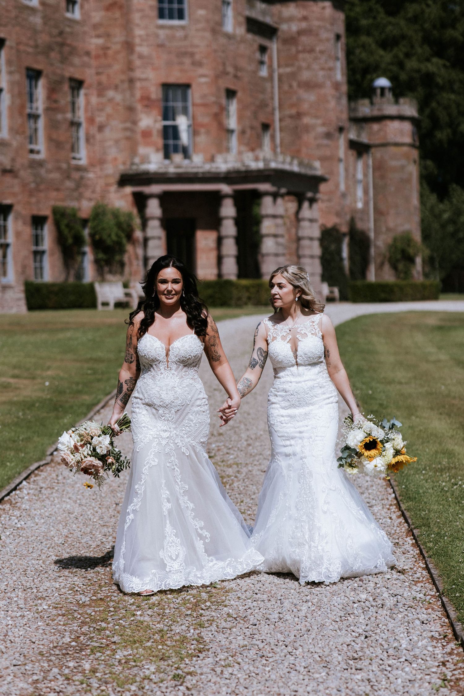 Fasque Castle Wedding Photography. Two wedding dresses sparkle on gravel path with historic brick building in background.