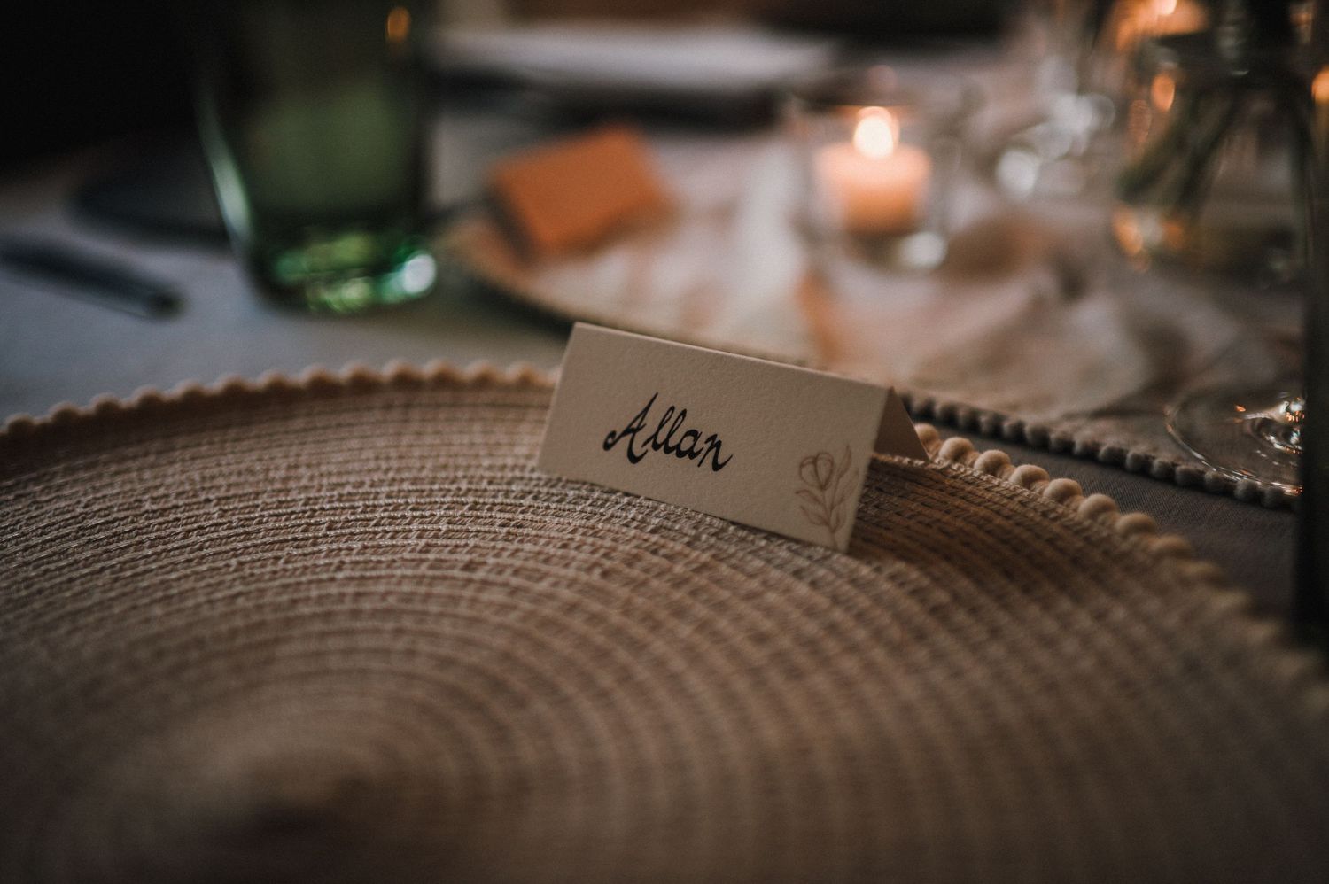 A wedding place card sits on a textured charger plate with soft candlelight.