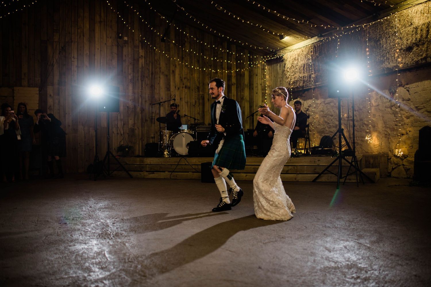 Newlyweds dance together in a romantic stone-walled venue illuminated by string lights.