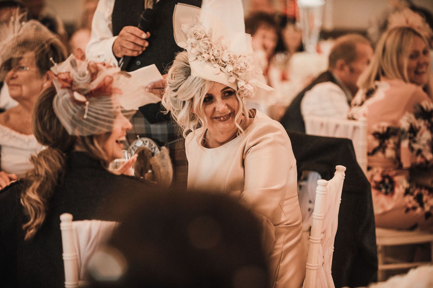 Guests share laughter during an elegant wedding reception with warm lighting.