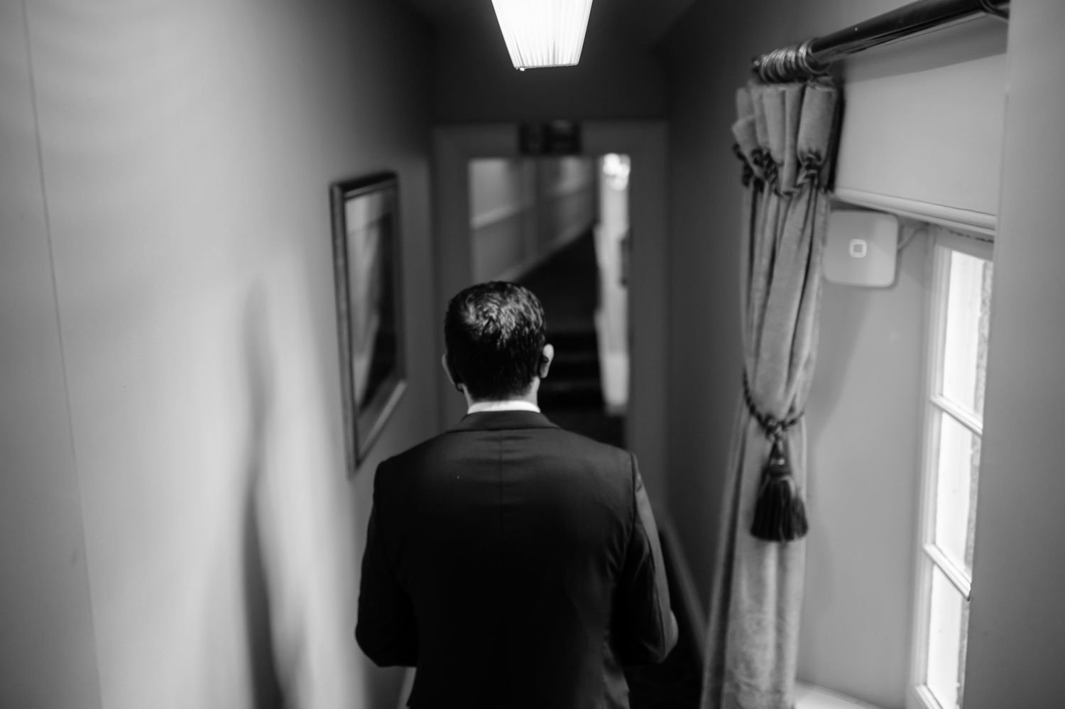 Black and white photo of person walking down narrow hallway from behind.