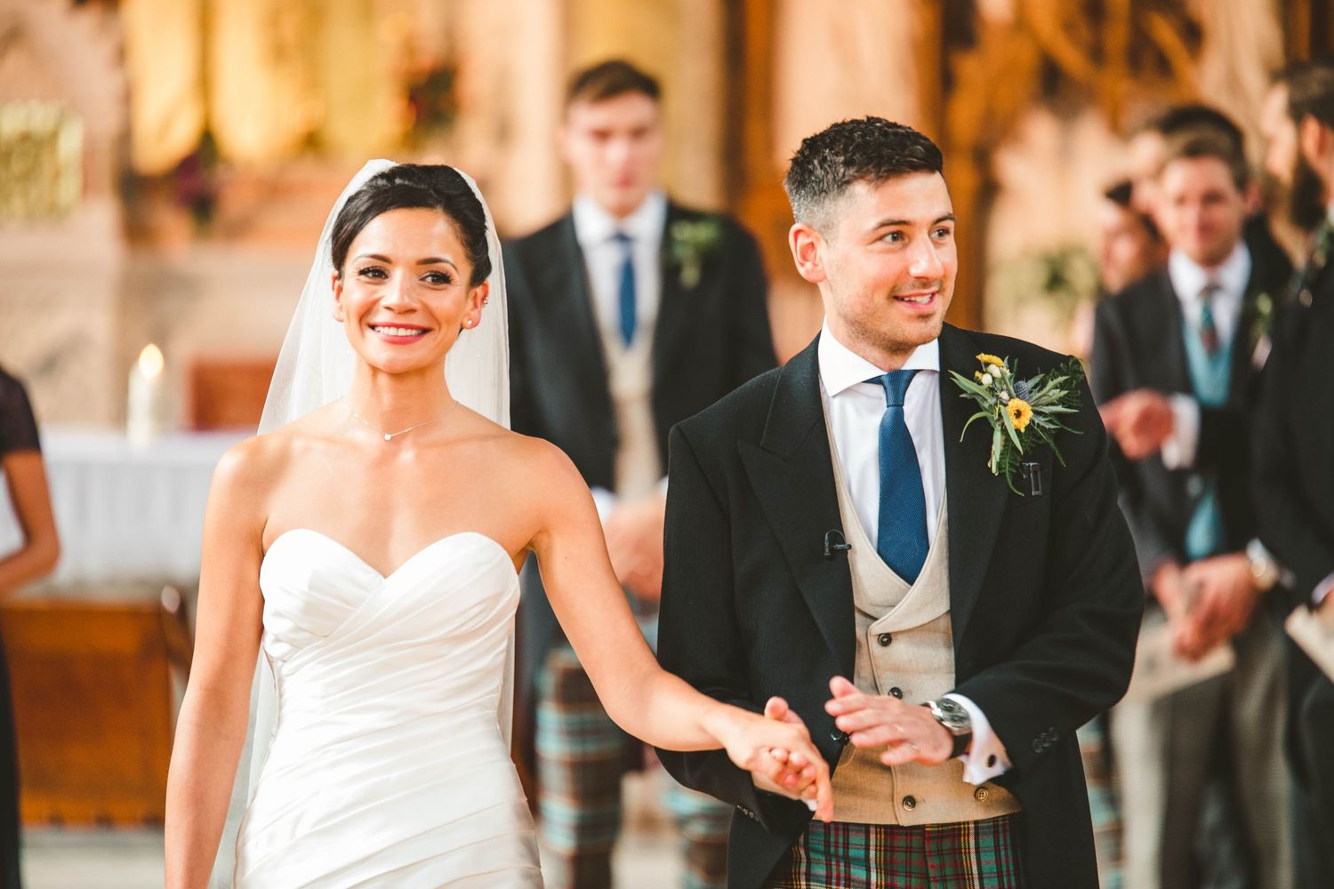 Newlyweds hold hands while walking down church aisle during their wedding ceremony.