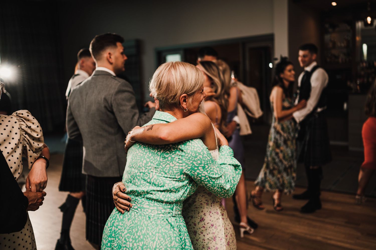 Two guests embrace on the dance floor during an evening wedding celebration.