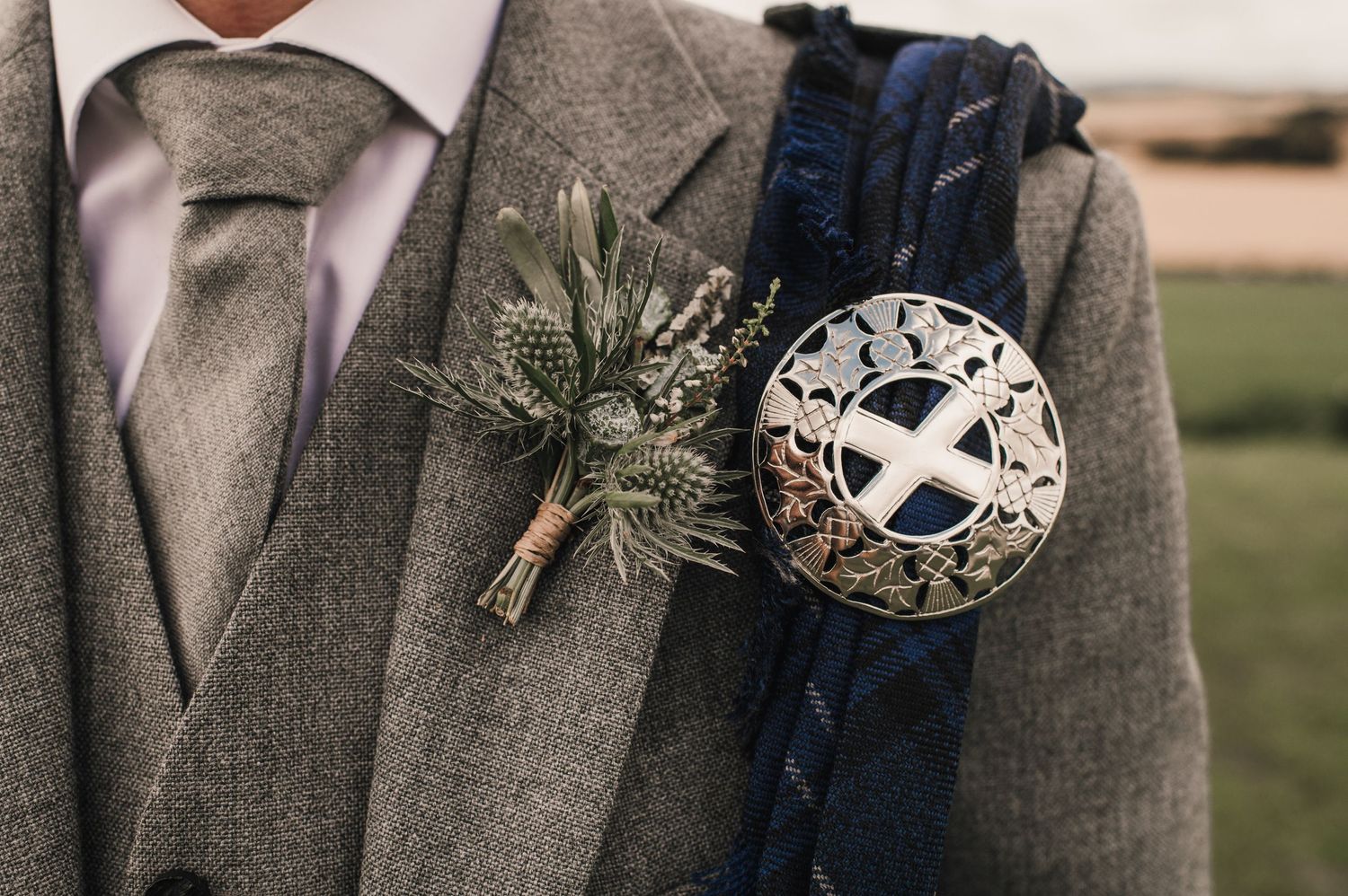 Close-up of a Scottish wedding boutonniere and saltire flag ball pin on a grey suit jacket.