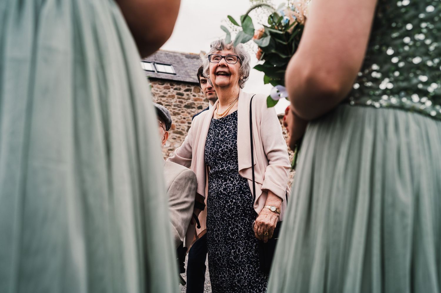 Guest in pale outfit laughs joyfully between mint green dresses at wedding celebration.