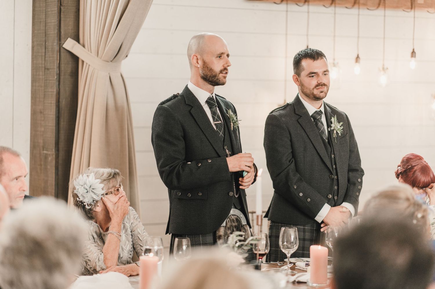Two people in formal attire deliver speeches at an elegant wedding reception.
