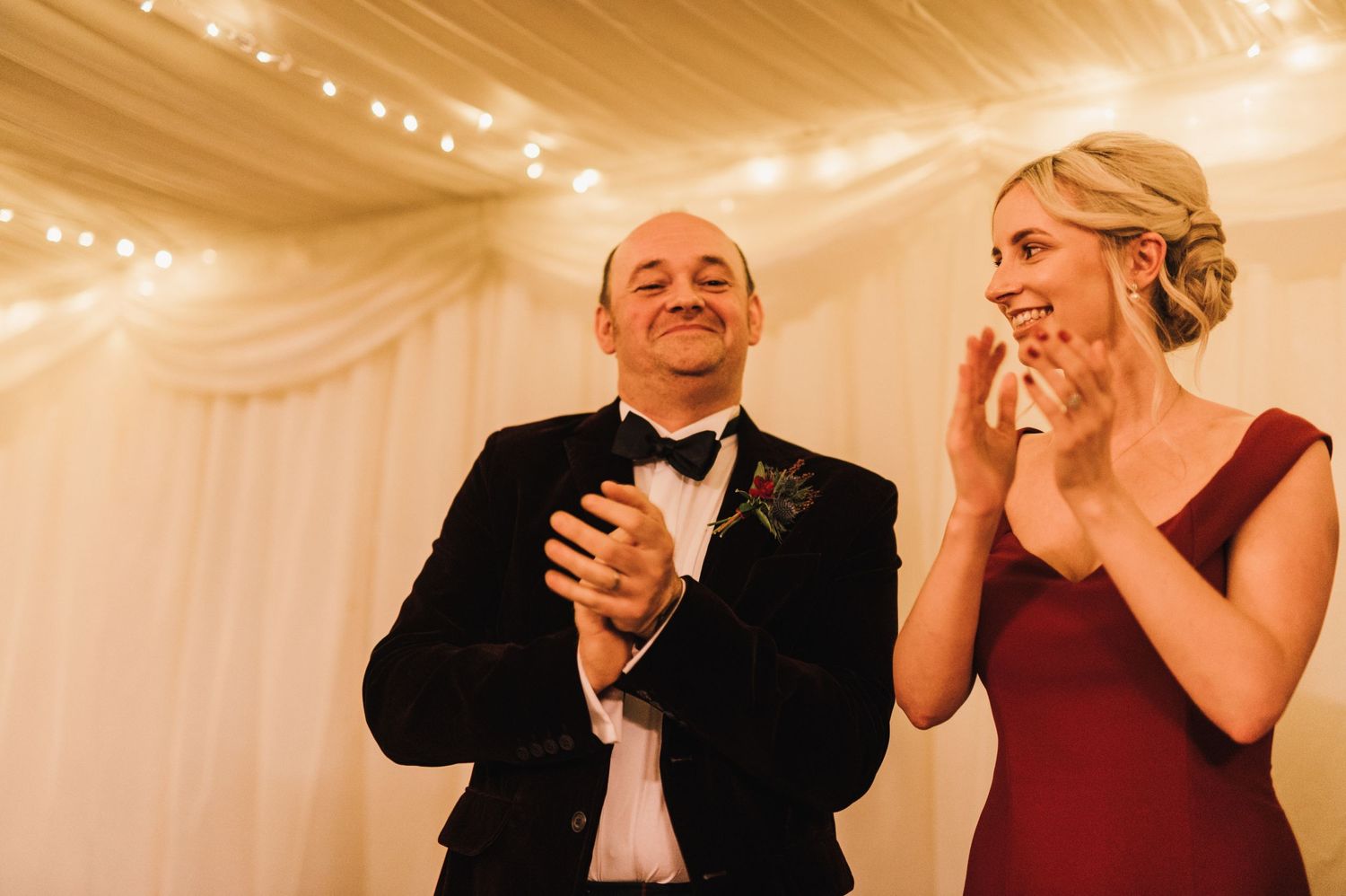 Emotional wedding reception moment with attendees reacting under draped white decor and string lights.