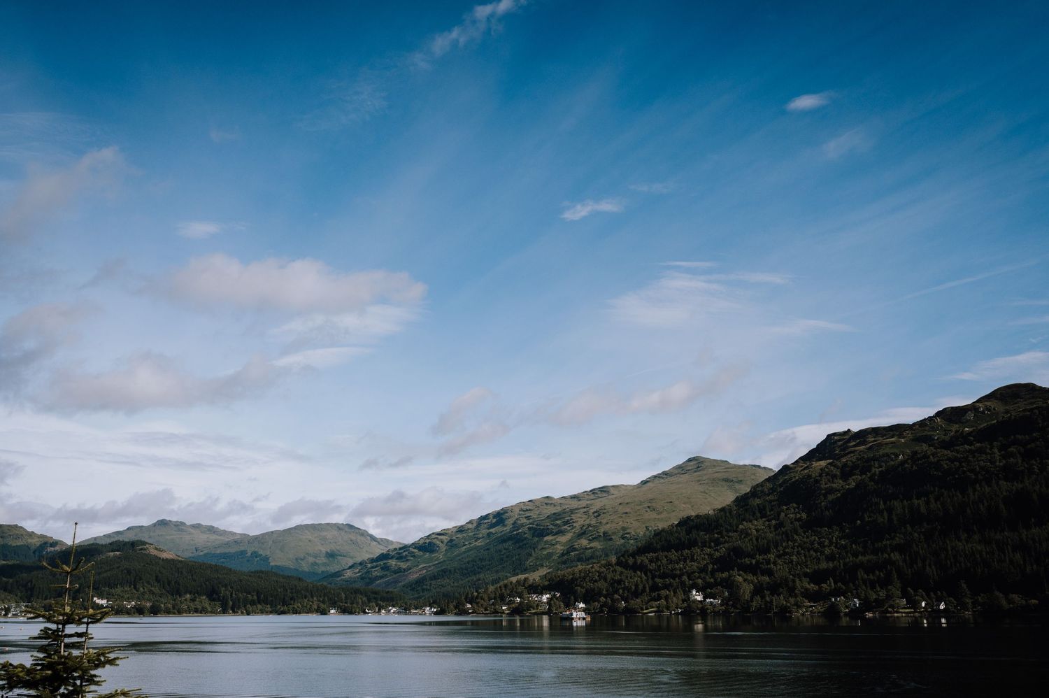 Scenic mountain lake landscape under blue skies with rolling hills and scattered clouds.