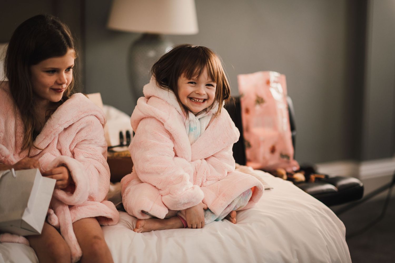 Wedding morning preparation scene with people in pink robes sitting on a bed.
