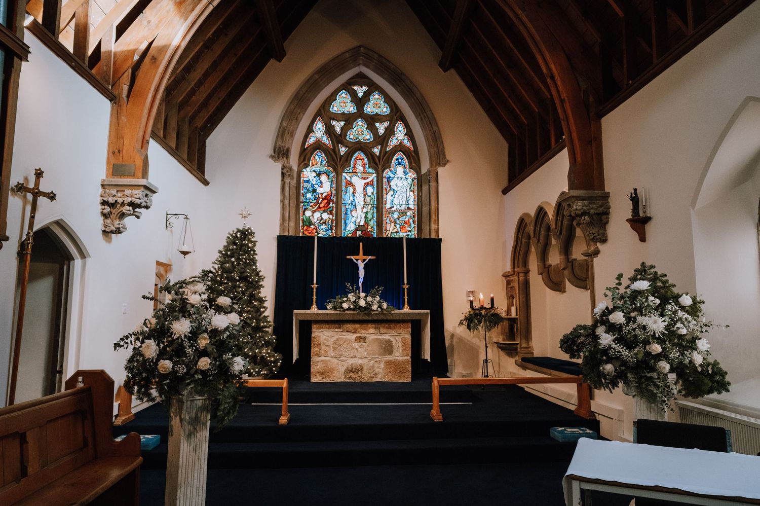 Gothic church interior with stained glass windows and floral arrangements at the altar.