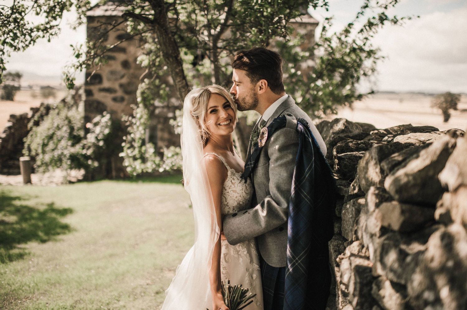 Romantic wedding portrait captured against rustic stone wall and greenery.