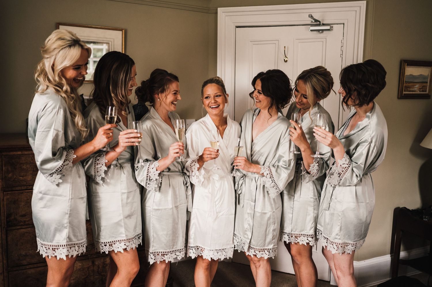 A group wearing matching gray lace-trimmed robes toast together during wedding preparations.