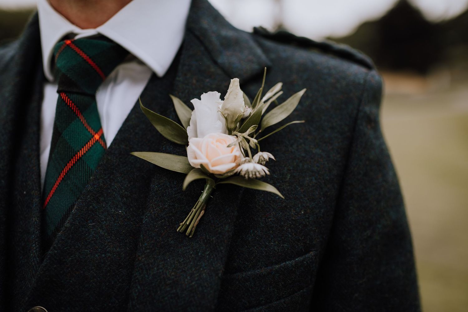 A delicate white rose boutonniere pinned to a dark suit jacket with green and red striped tie.