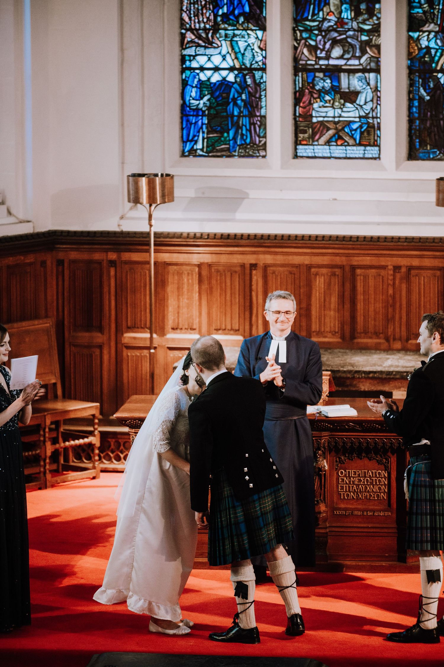 Traditional Scottish wedding ceremony taking place on red carpet in church sanctuary.