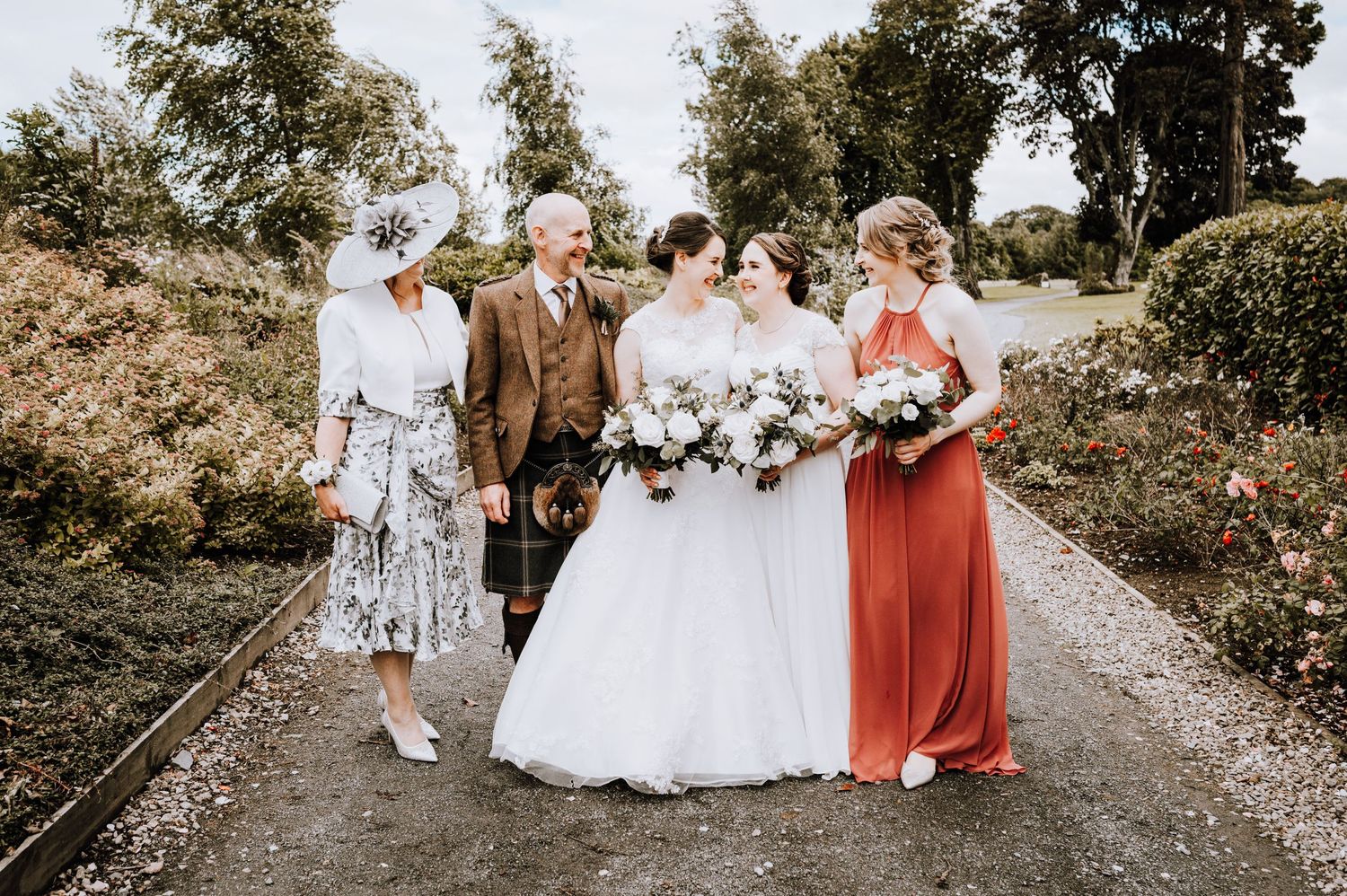 Wedding group portrait on a garden path with people in formal attire and floral dresses.
