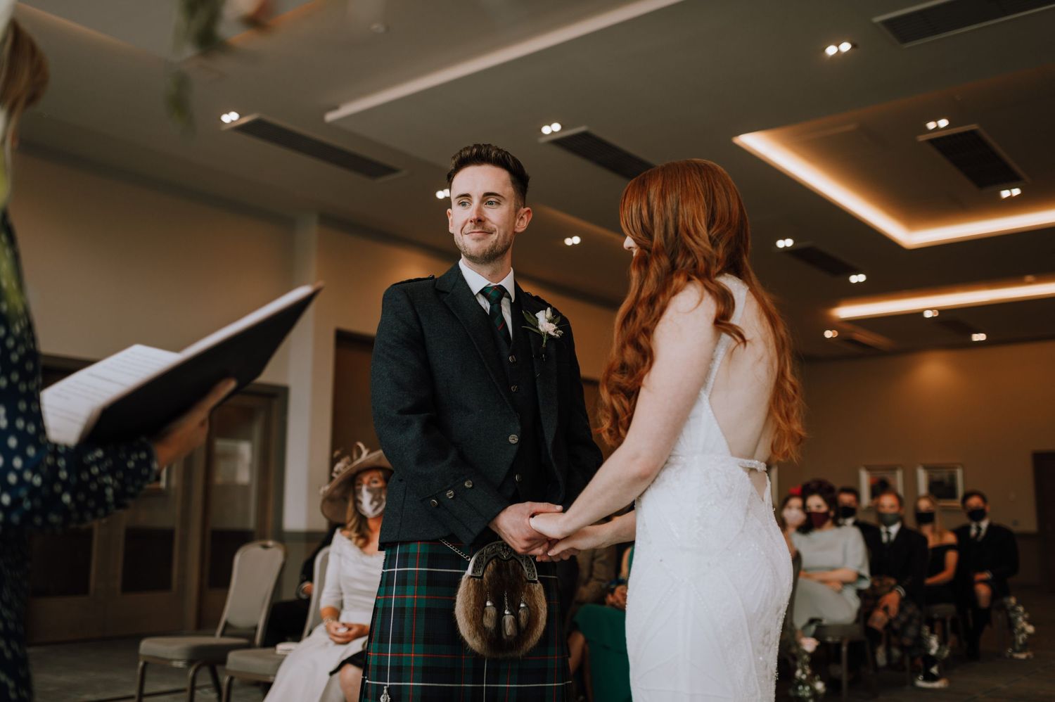 Traditional Scottish wedding ceremony with groom in kilt and bride in white dress.