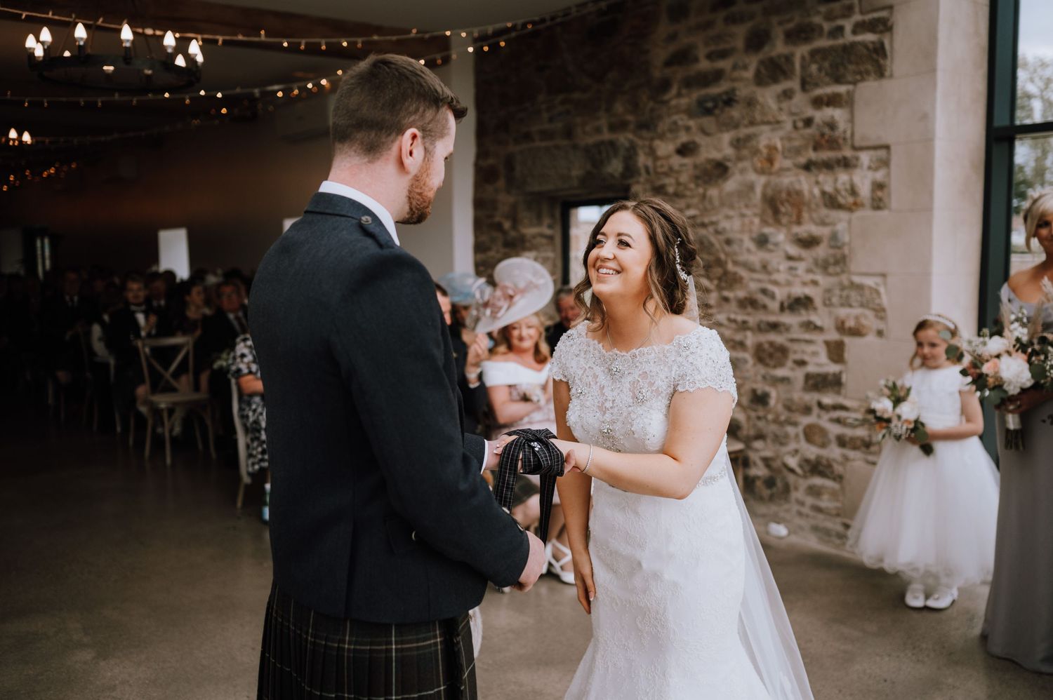 Joyful moment during wedding ceremony in rustic venue with string lights and stone walls.