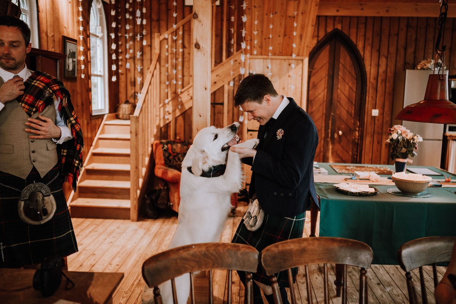 Two people celebrate together inside a rustic wooden interior with a staircase and twinkle lights.