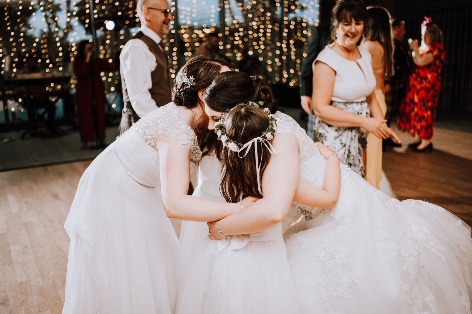 Wedding celebration with guests dancing in an indoor venue decorated with string lights.