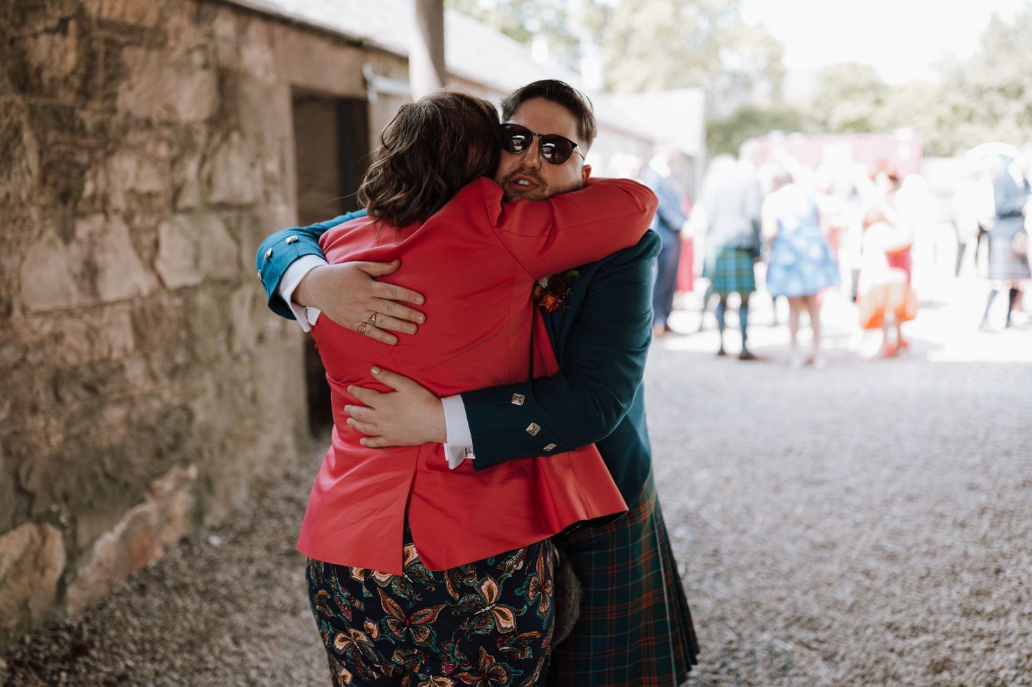 Two guests share warm embrace at outdoor Scottish wedding celebration.