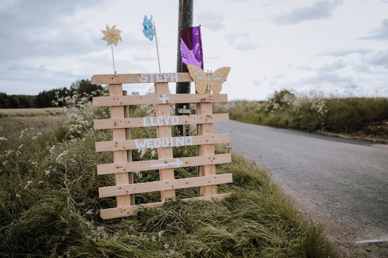 A rustic wooden pallet decoration with colorful flags along a country road.
