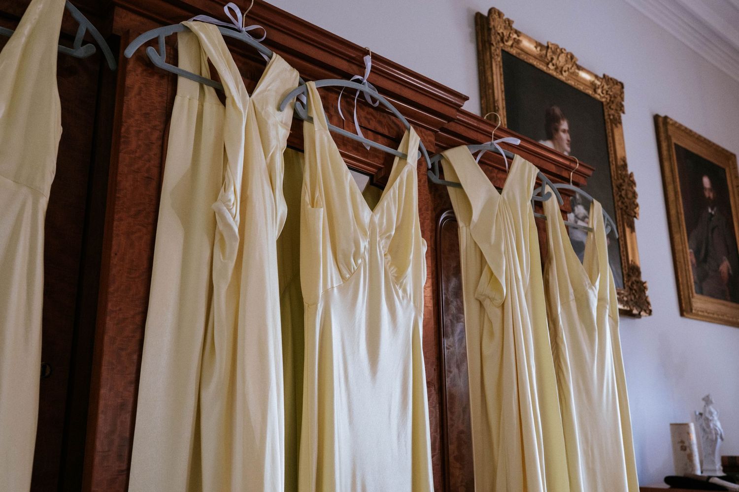 Row of cream colored bridesmaid dresses hanging on wooden hangers.